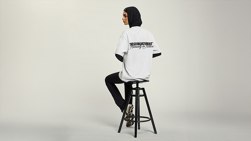 Woman in a black hijab and oversized white T-shirt sitting on a stool in a minimalist studio